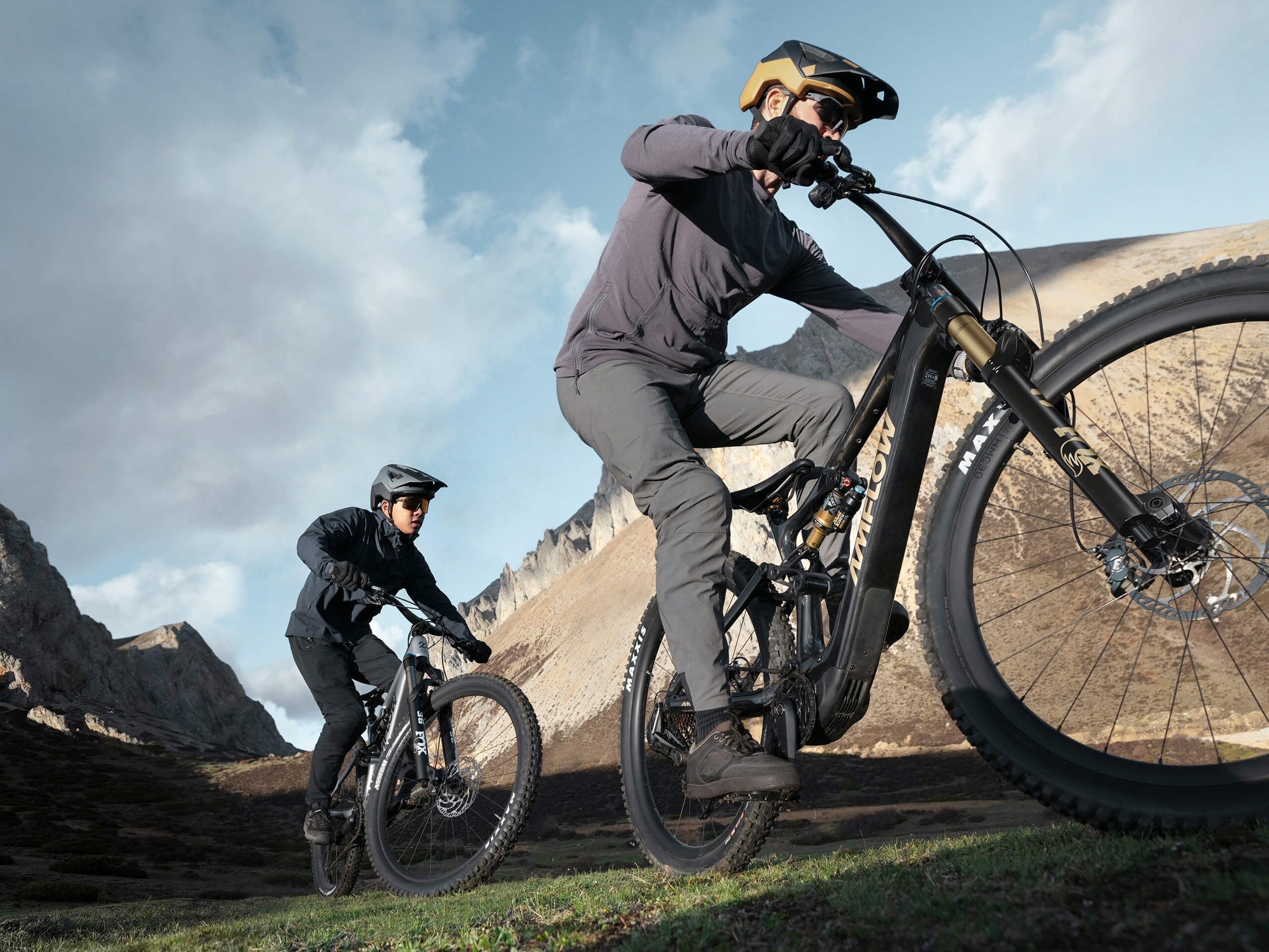Two mountain bikers riding on a trail with mountains in the background