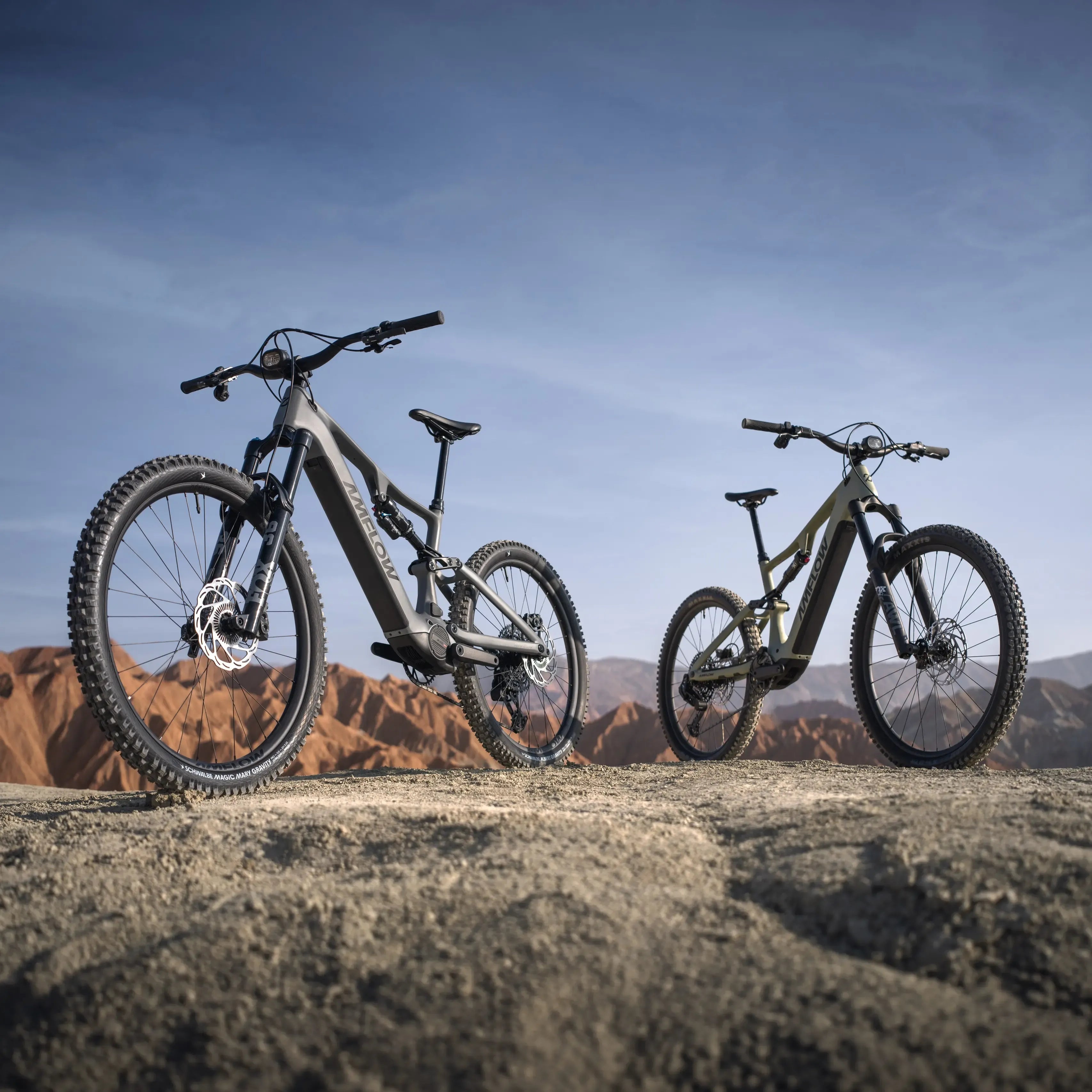 Two electric Amflow Mountain Bikes on a rocky surface with a mountainous background