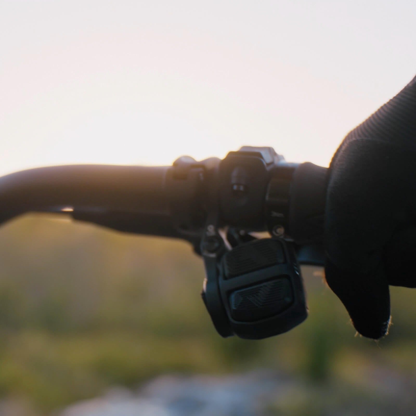 Gloved hand holding mountain bike handlebar with an electric controller against a blurred background