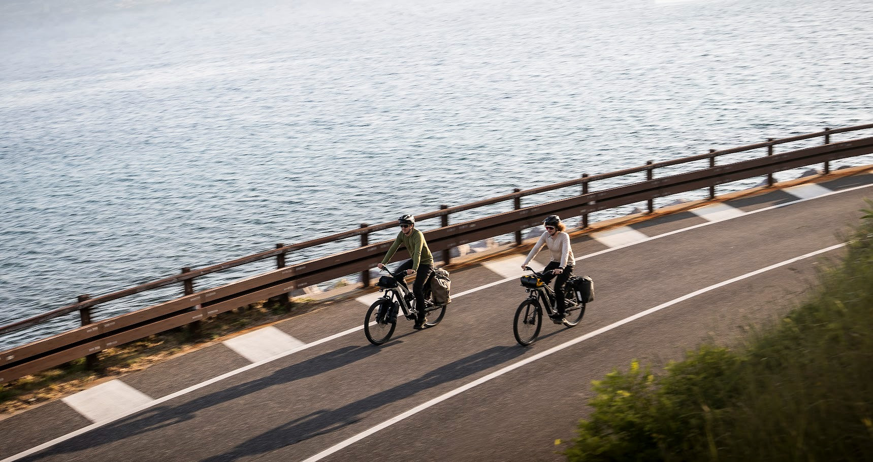 Two cyclists riding along a scenic road by the water.