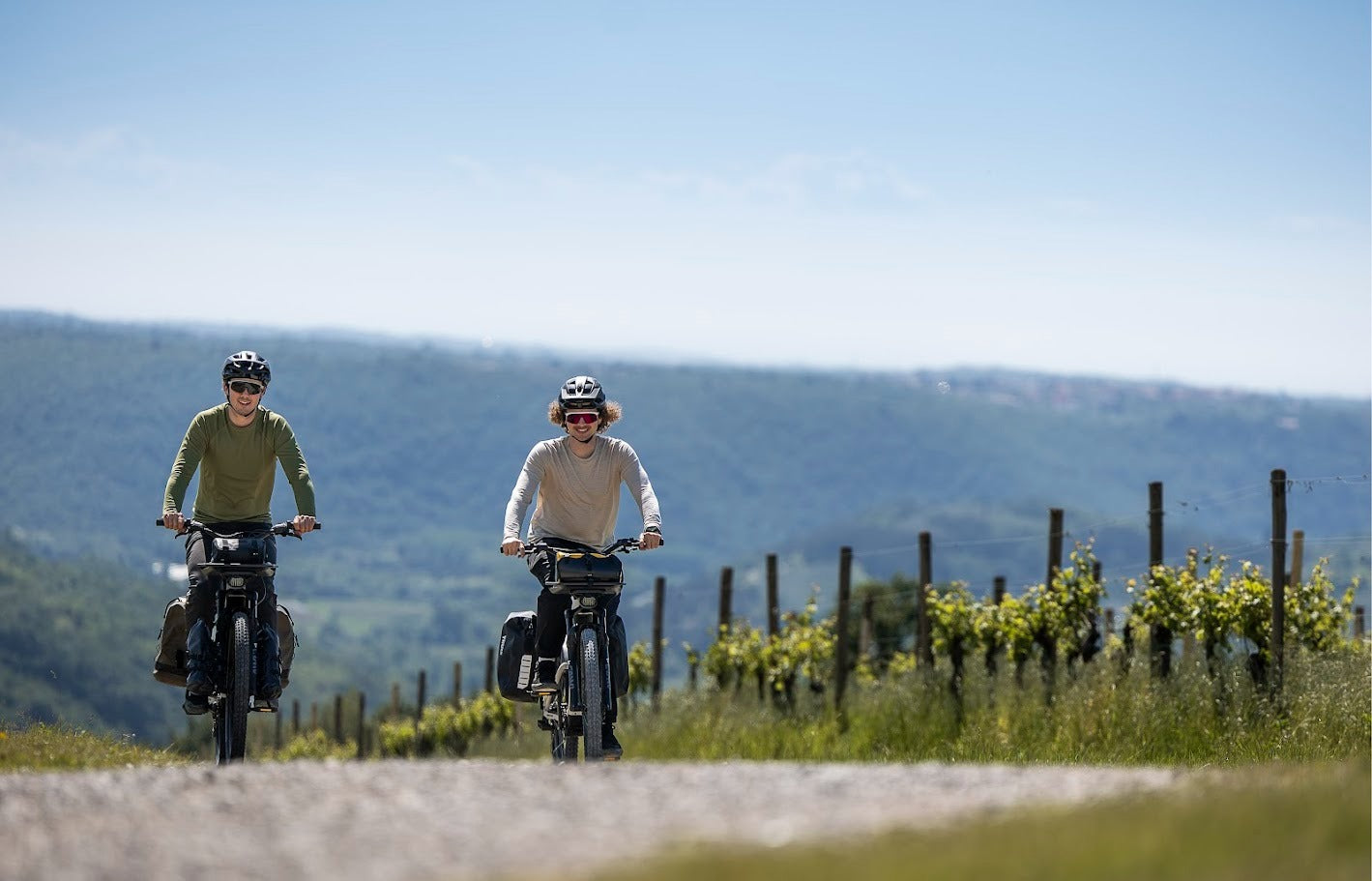 Two people riding electric bikes on a scenic road with mountains in the background