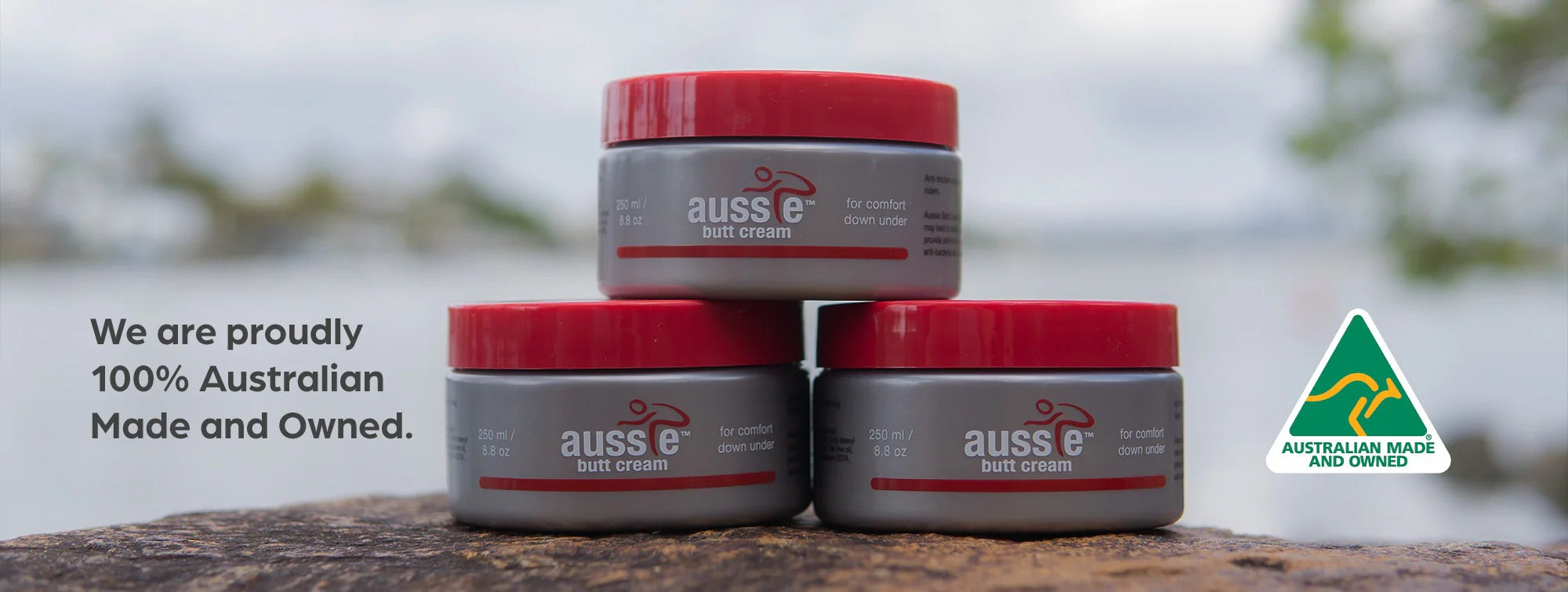 Three jars of Aussie Butt Cream with red lids on a wooden surface, Australian Made logo visible