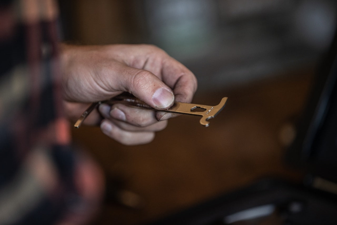 A hand holding a bicycle chain checker with blurred workshop in the background