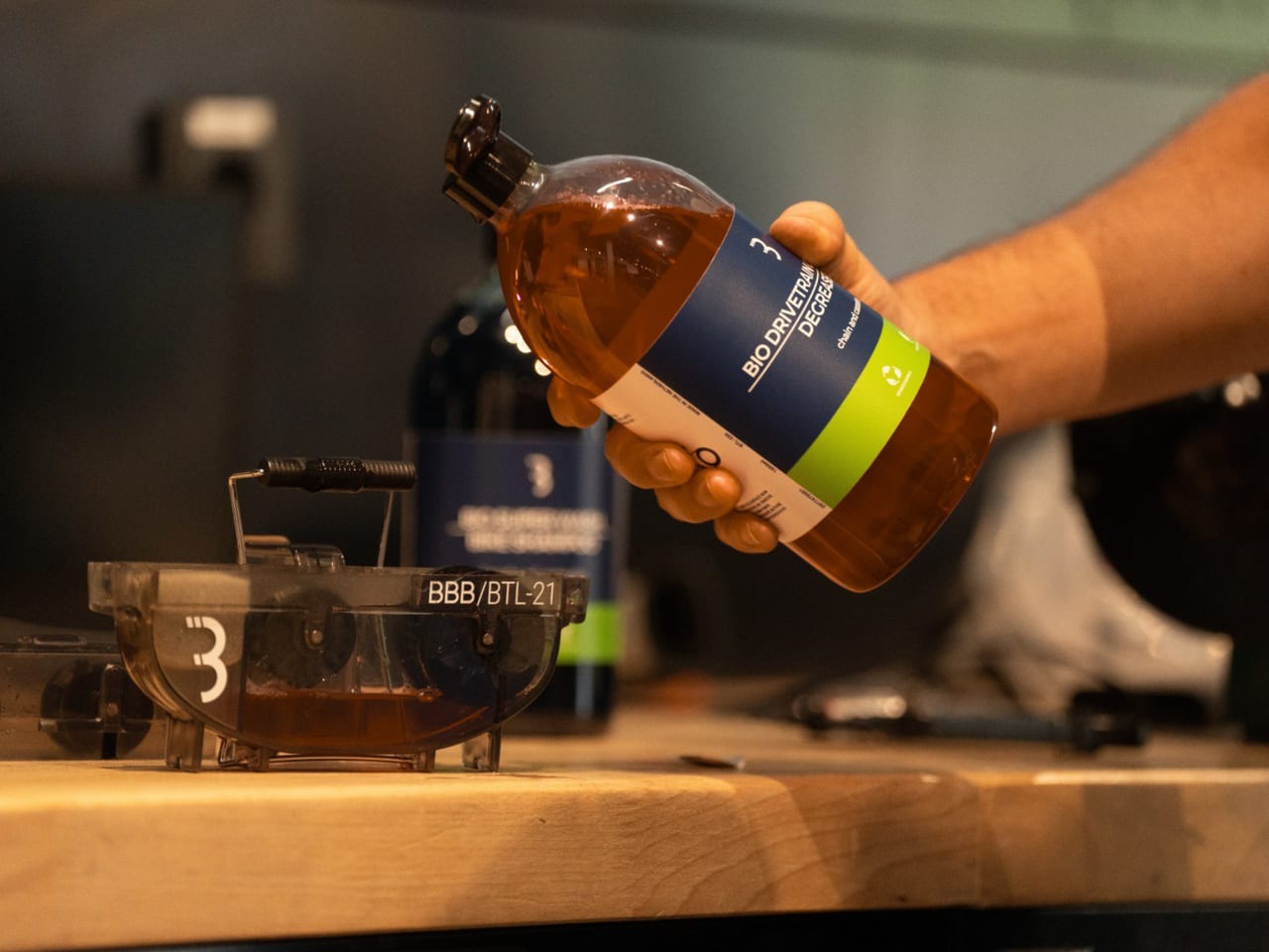 A person filling a BBB Chain Cleaner with Degreaser fluid with a workshop bench in background