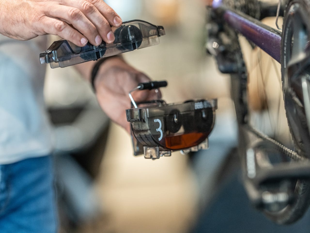 Person working on a bicycle with close-up of hands pulling a chain cleaner tool apart on a blurred background