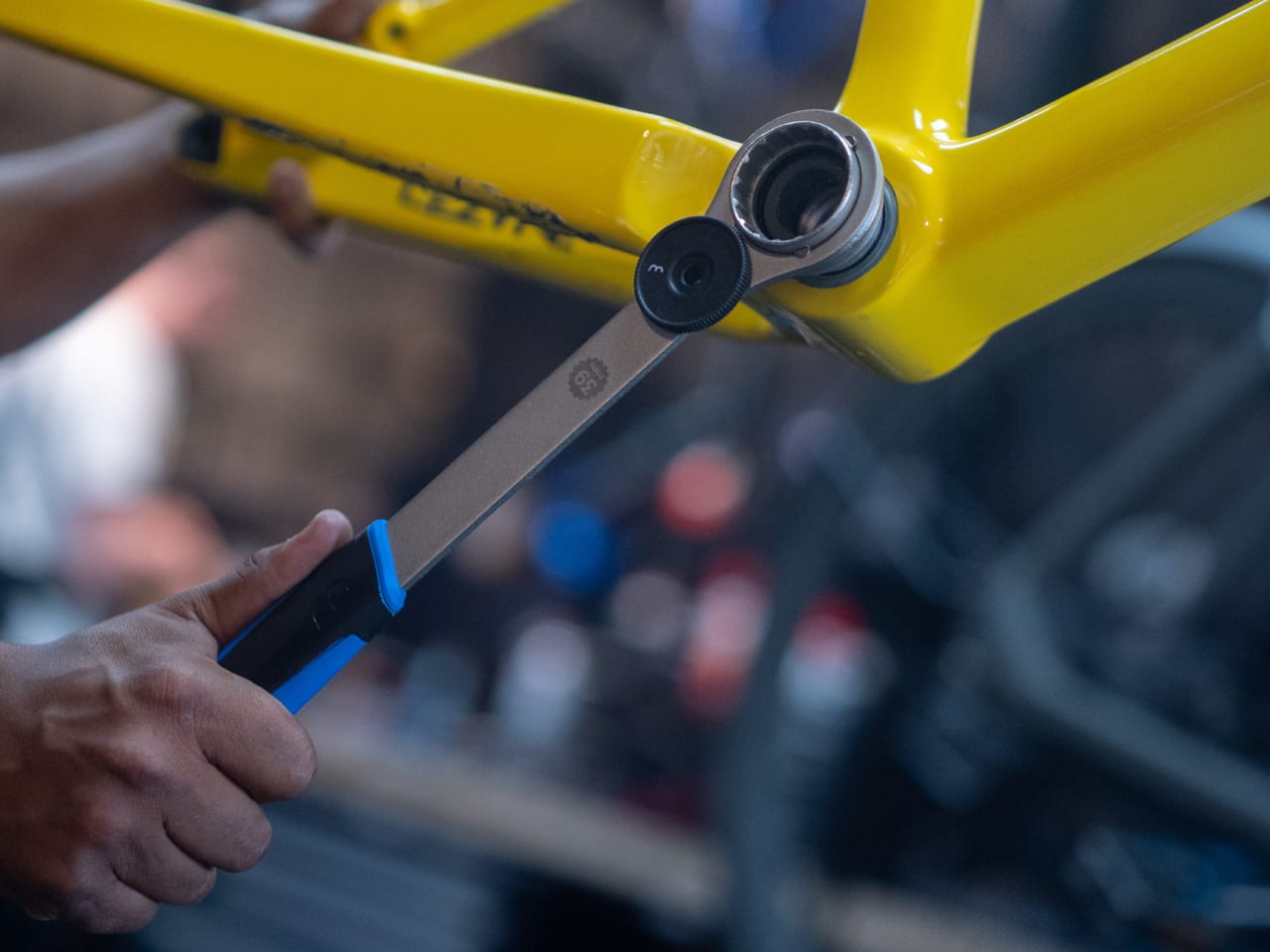 Person using a bottom bracket tool on a yellow bicycle frame with a blurred background