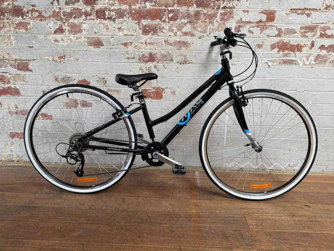Black bicycle with white rims and blue accents against a brick wall.