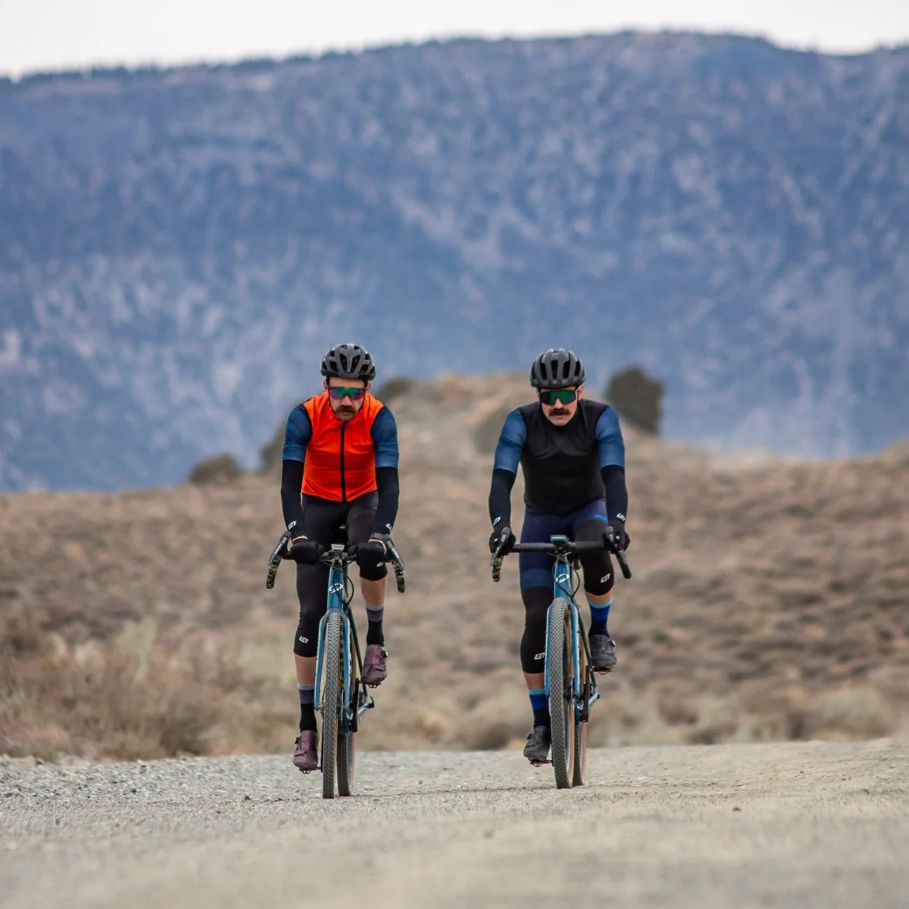 Two cyclists riding on a gravel road with mountains in the background