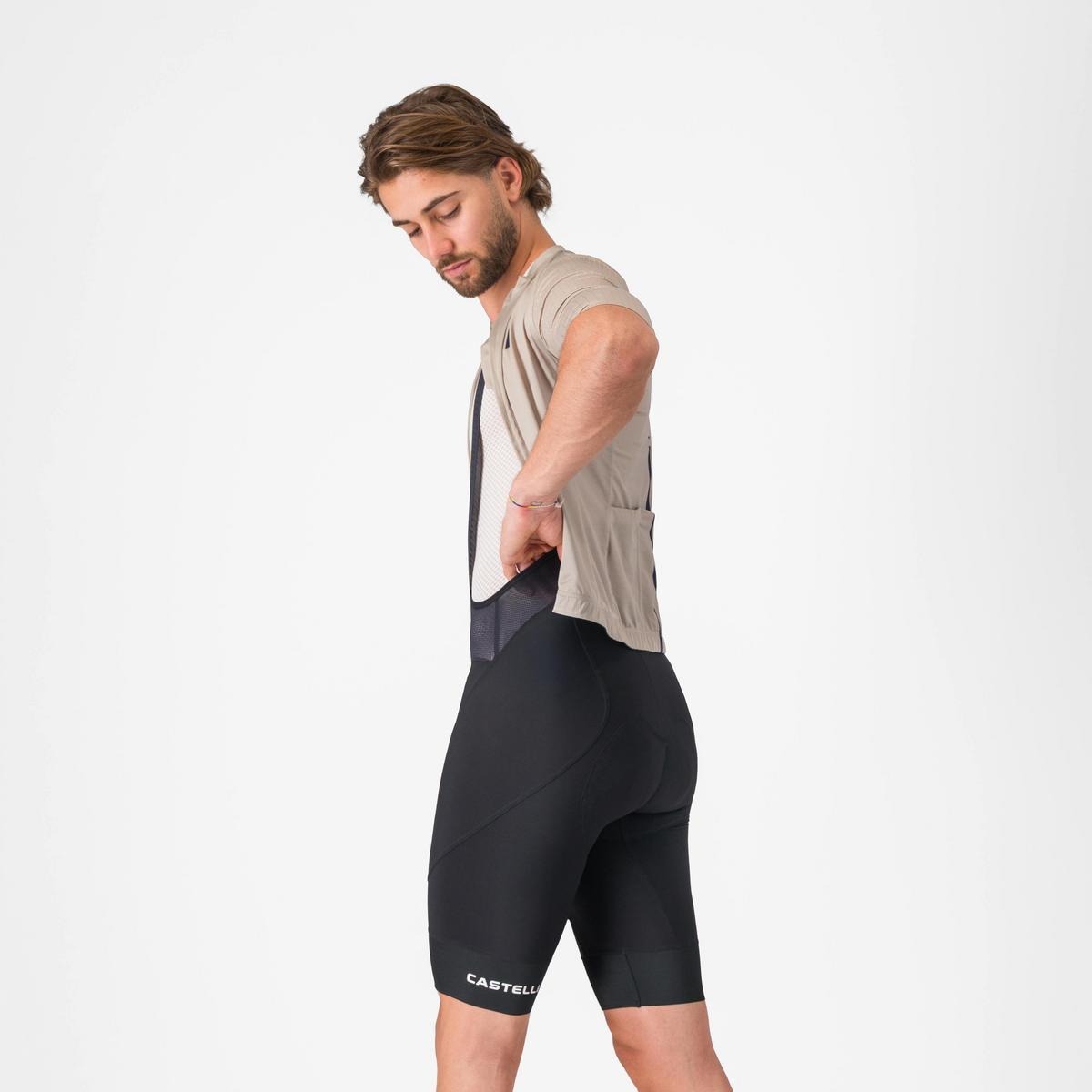 A side view of someone wearing cycling bibshorts and jersey on a light grey background