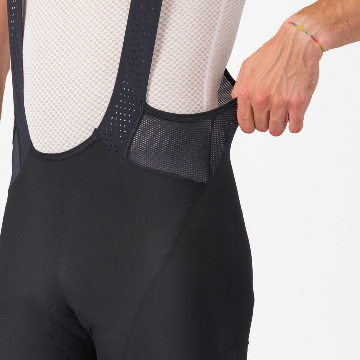 A close up of someone wearing cycling bibshorts showing the waist section on a light grey background