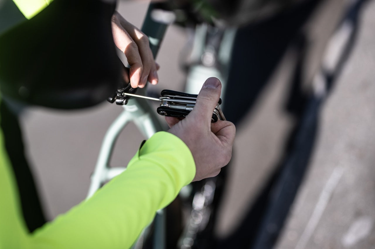 Close up of a person installing a bicycle seat post clamp using a multi tool on a blurred background