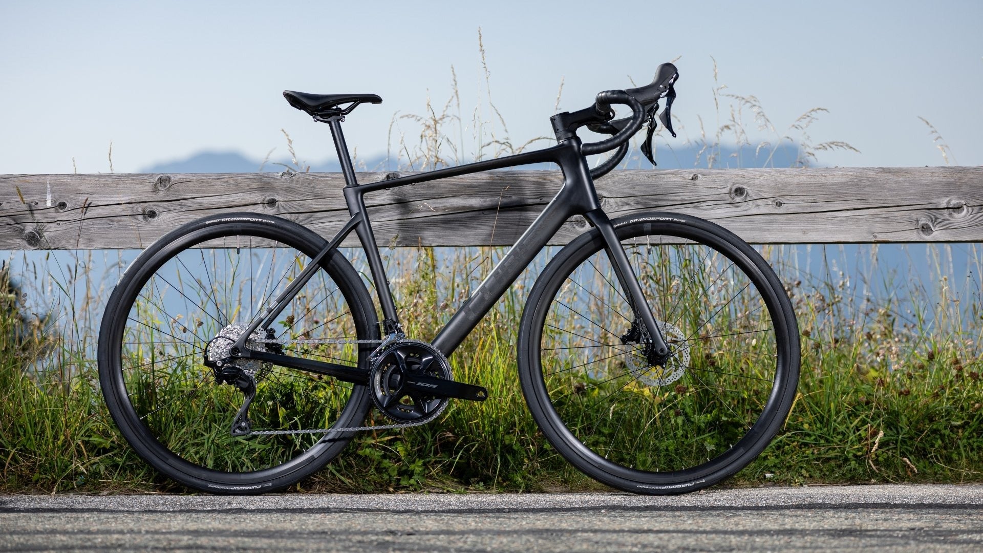 Black bicycle leaning against a wooden fence with a scenic background