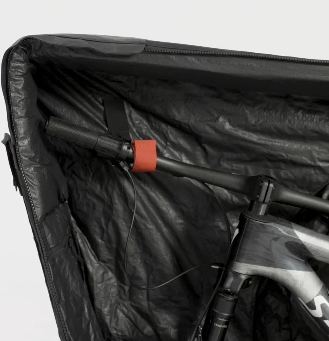 Bicycle inside a black protective case with a red strap on a light gray background