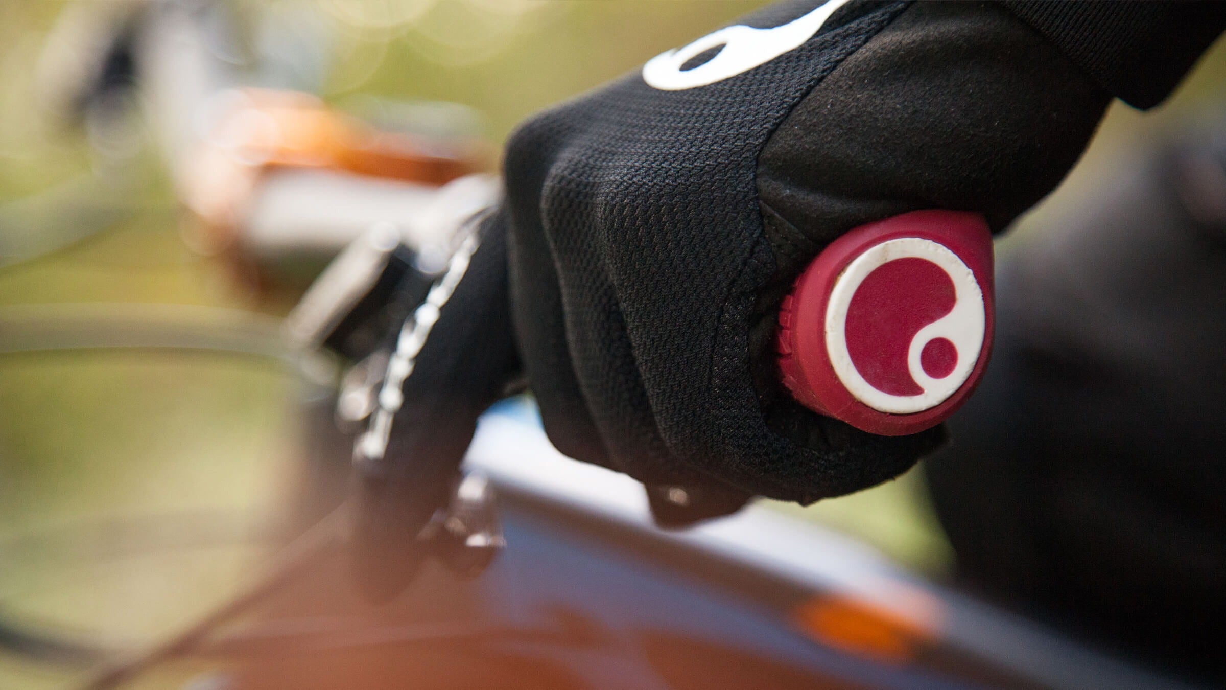 Close-up of a gloved hand gripping a bicycle handlebar with a brand logo.