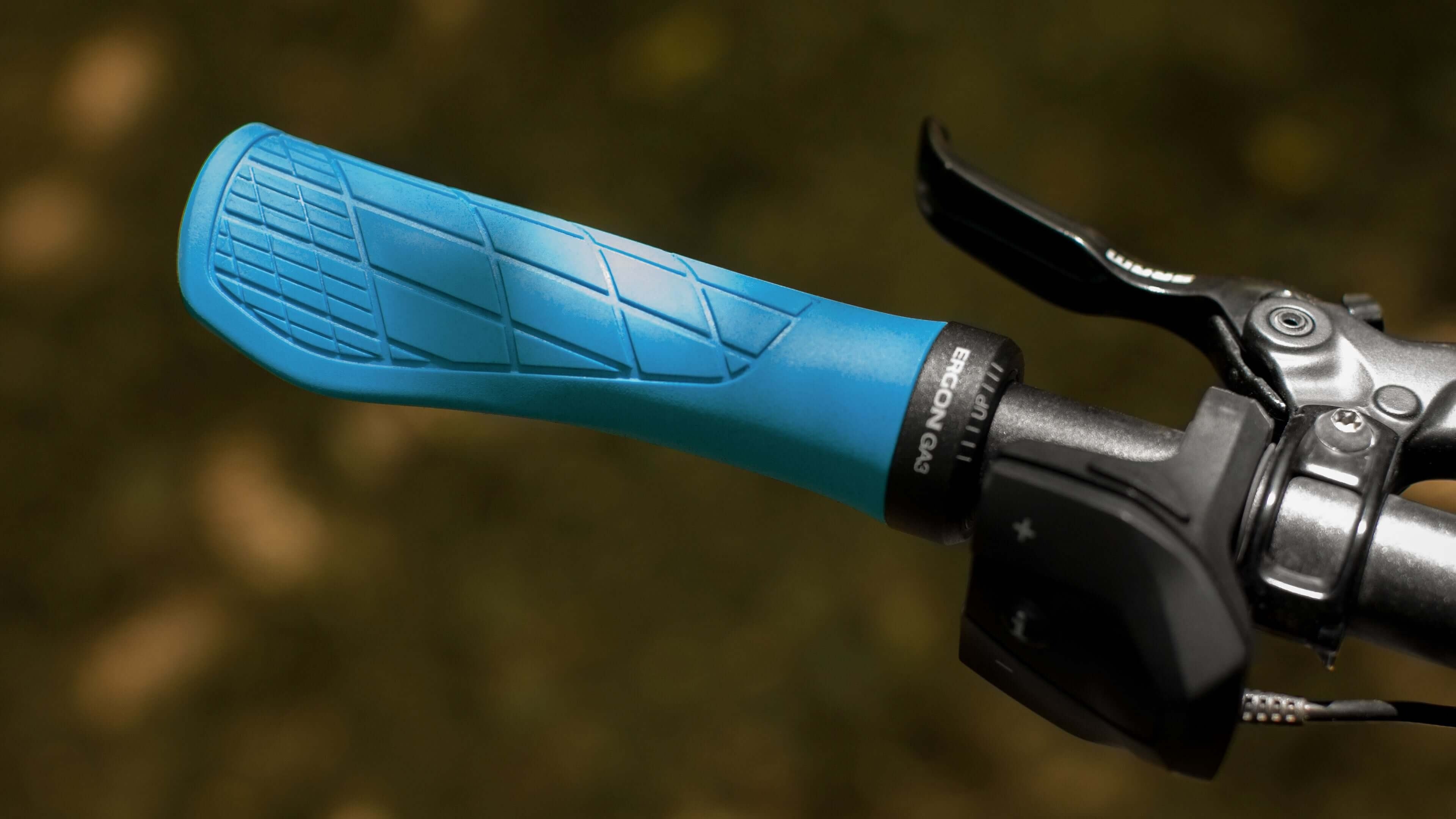 Close-up of a blue bicycle handlebar grip and black brake lever against a blurred natural background