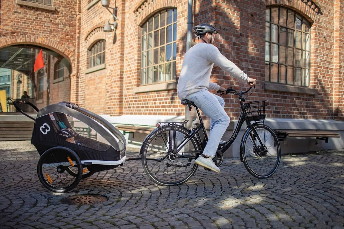 A man riding a bike towing a child in a bike trailer with an urban background