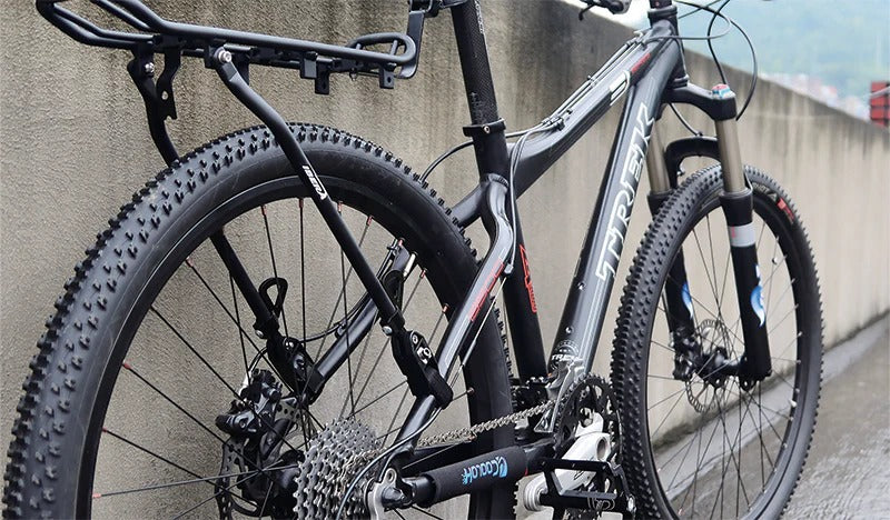A mountain bike with a pannier rack attached leaning against a concrete wall