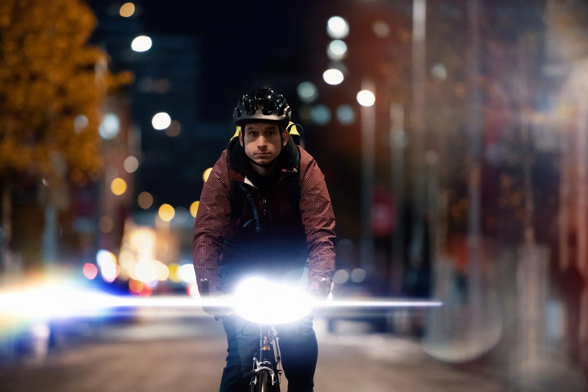 Cyclist on a city street at night with a bright headlight illuminating the path.
