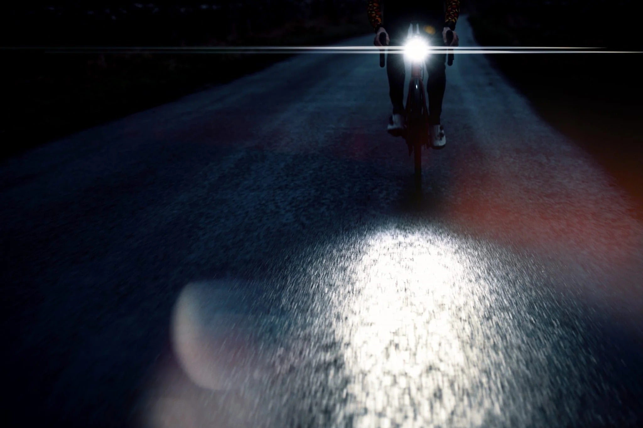 Person riding a road bike on a dark road with a bright headlight.