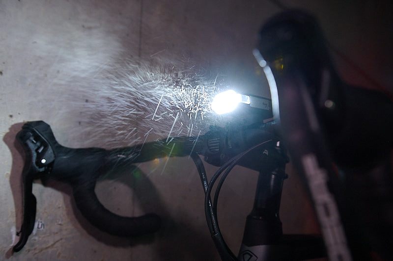 Bicycle light shining in the dark mounted on road bike handlebars with a concrete wall in the background