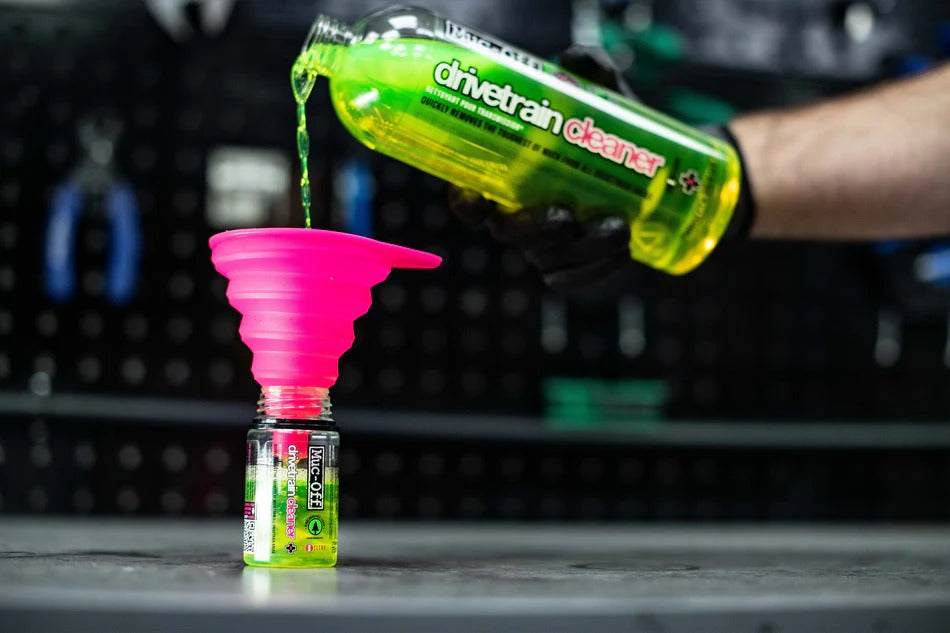 Muc-Off Drivetrain cleaner being poured into a small container using a pink funnel.