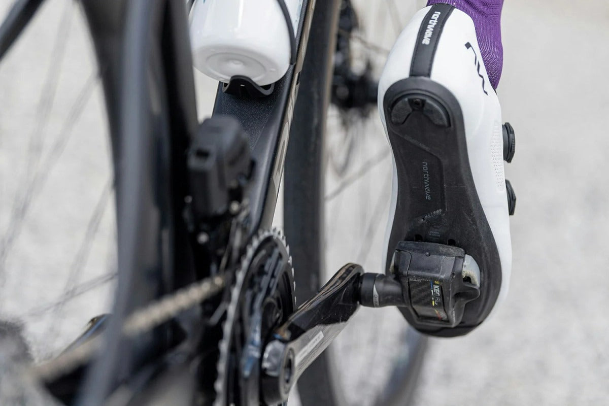 White cycling shoes attached to a bicycle pedal with a blurred background