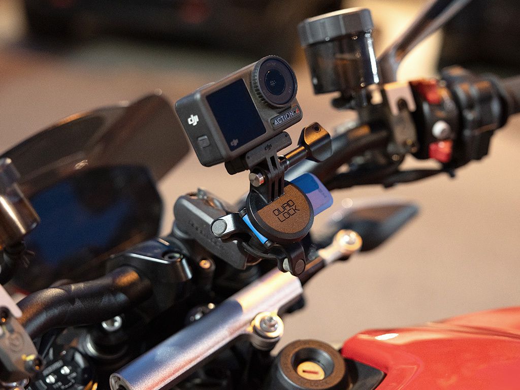 A close up of the handlebar of a motorbike with a Quad Lock camera mount and camera on handlebar