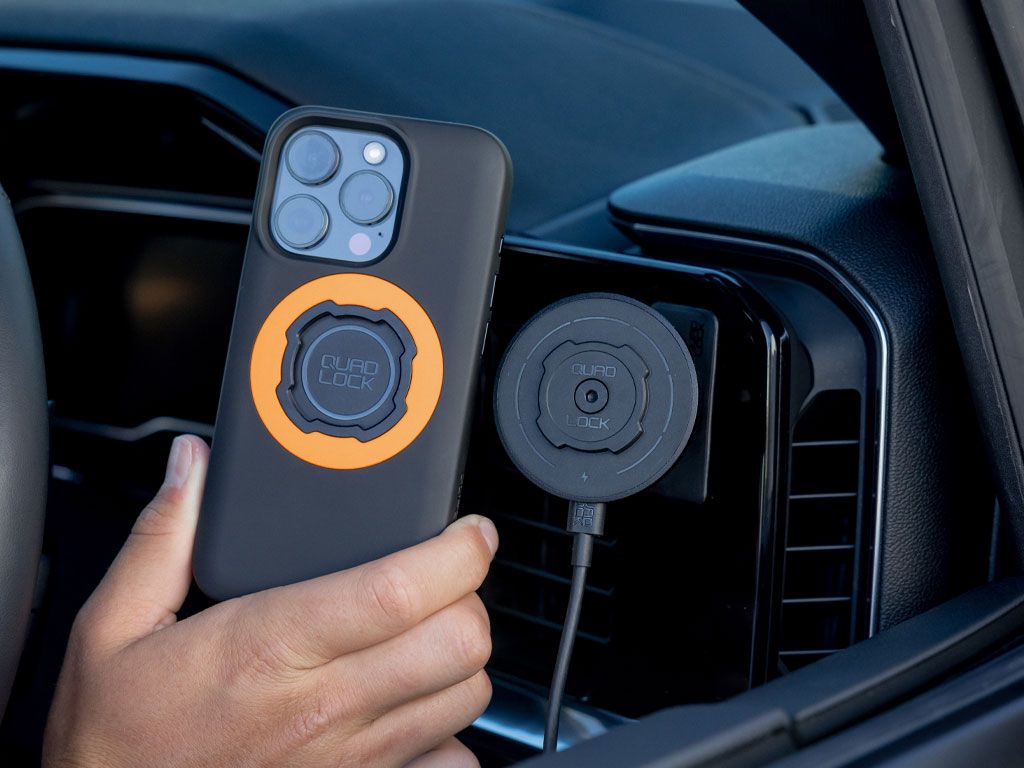 Person holding a phone with a magnetic Quad Lock phone case and car mount attached inside a vehicle.