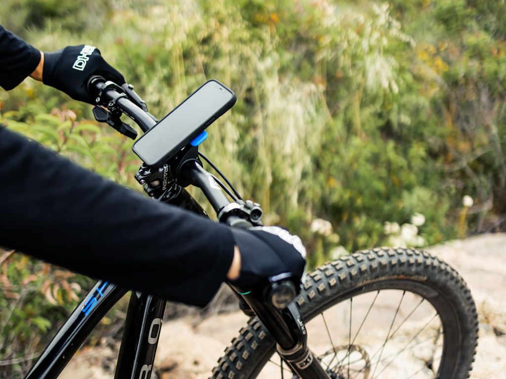 Person holding a mountain bike with a smartphone mounted on the handlebar against a natural background