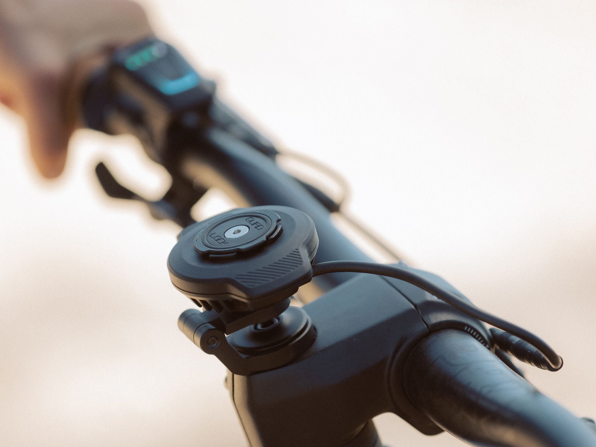 Close-up of a bike handlebar with a Quad Lock bike mount attached to the stem on a blurred background