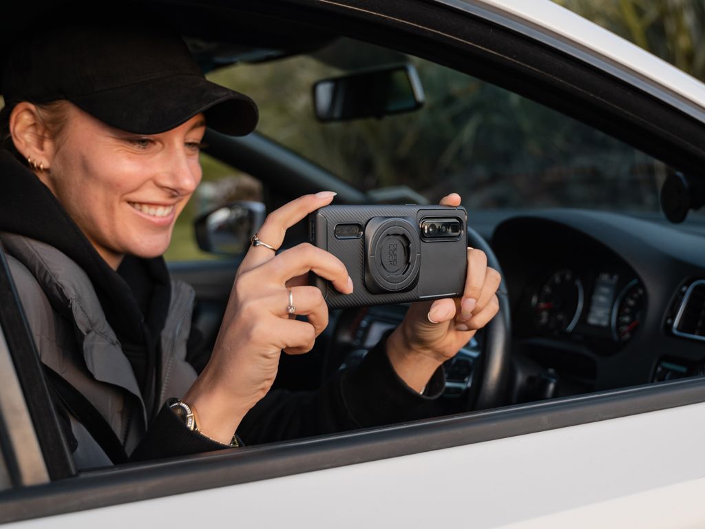 Person inside a car holding a phone with a Quad Lock Phone Case taking a photo and smiling.