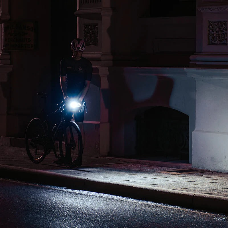 Person with a road bike and bright front light on a dark street at night