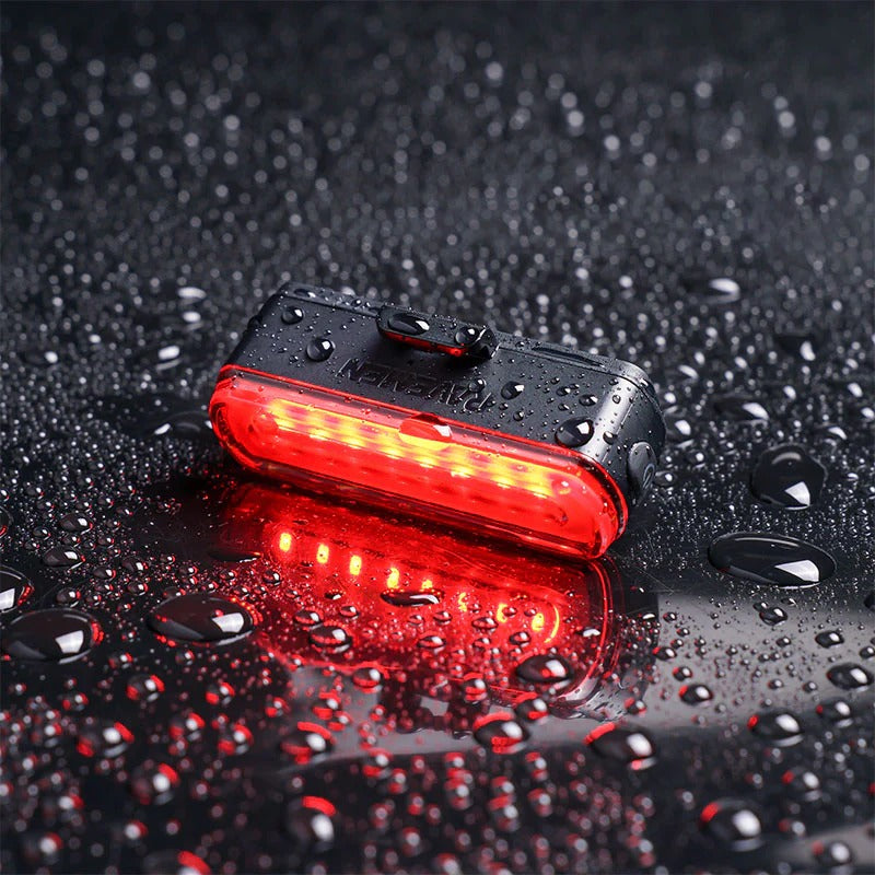 Red bicycle tail light on a wet surface with water droplets.