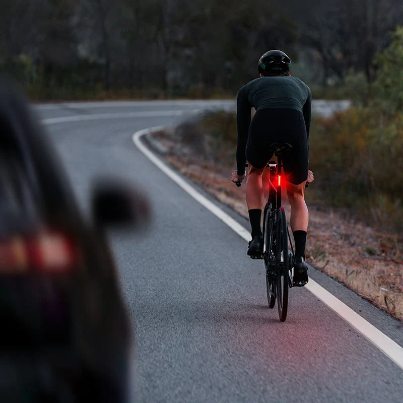 Cyclist riding on a road with bright red tail light on bike with a car following from behind