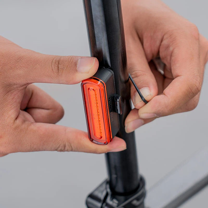Close-up of hands attached a red tail light on a bicycle seatpost on a grey background