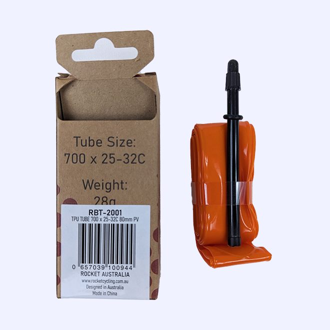 A Rocket bicycle inner tube shown next to its cardboard retail box on a plain light background. The tube is bright orange with a black valve stem, and the box is brown kraft paper with printed tube size and weight information.