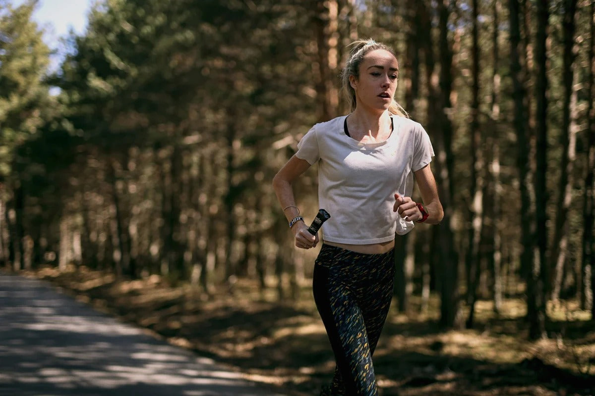 A lady running holding a SIS Beta Fuel in her hand with a forest in the background
