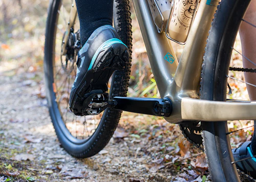 Close-up of a person riding a bicycle on a trail with focus on the foot and bike frame.