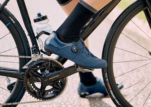 Close-up of a person wearing blue cycling shoes on a bicycle.