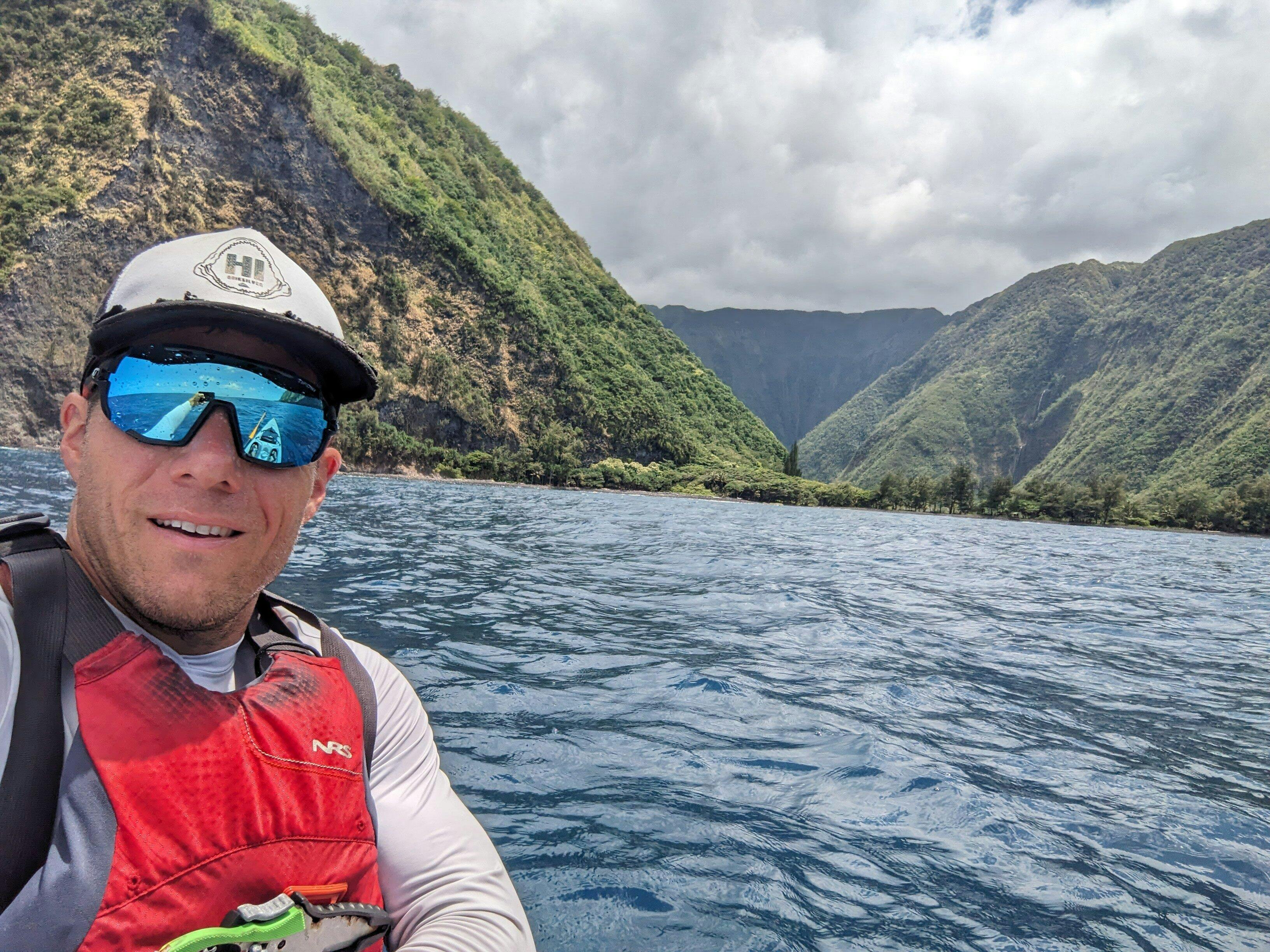 Man on a boat wearing a life jacket and sunglasses with mountains in the background