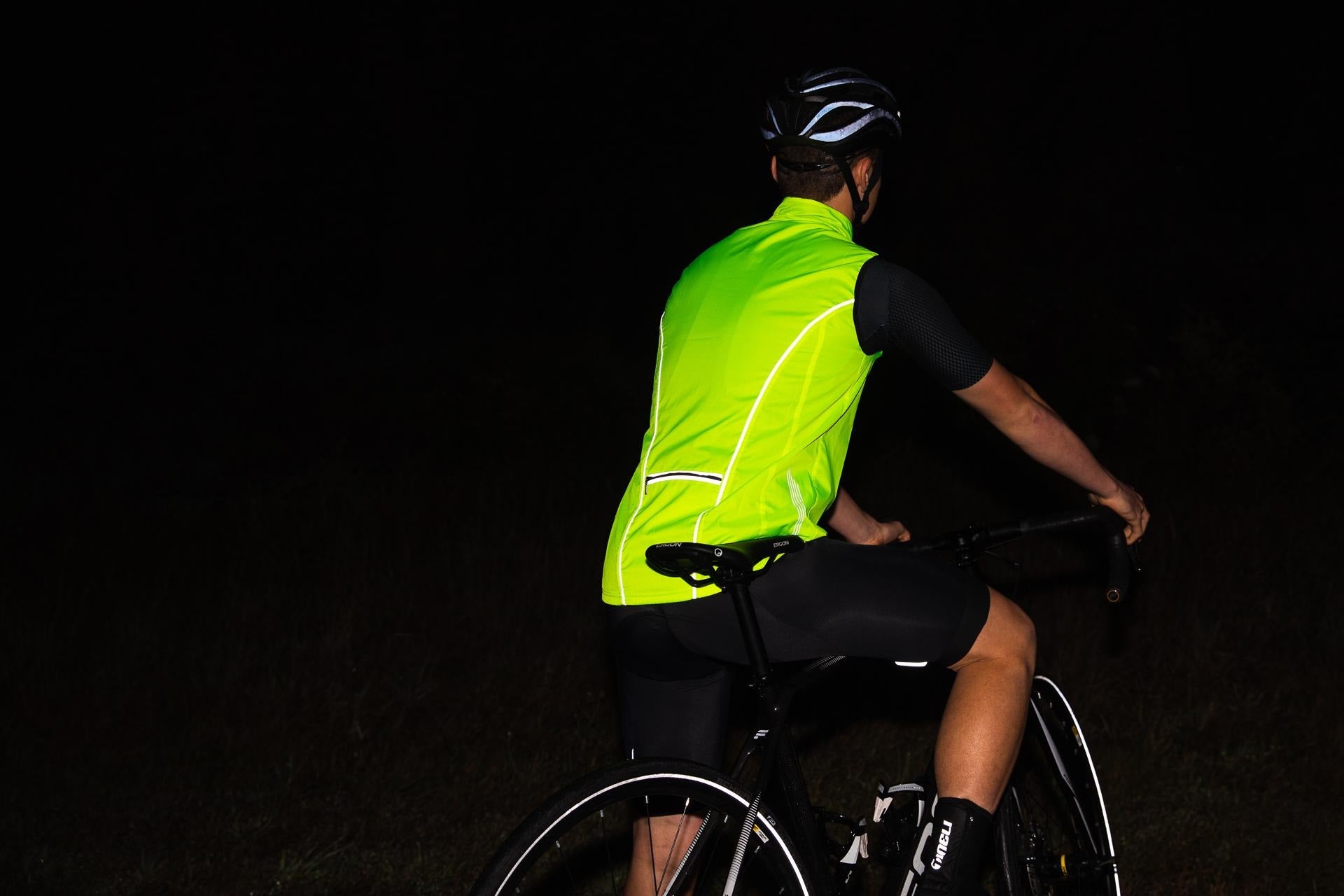 Person cycling at night wearing a bright yellow safety vest and helmet.