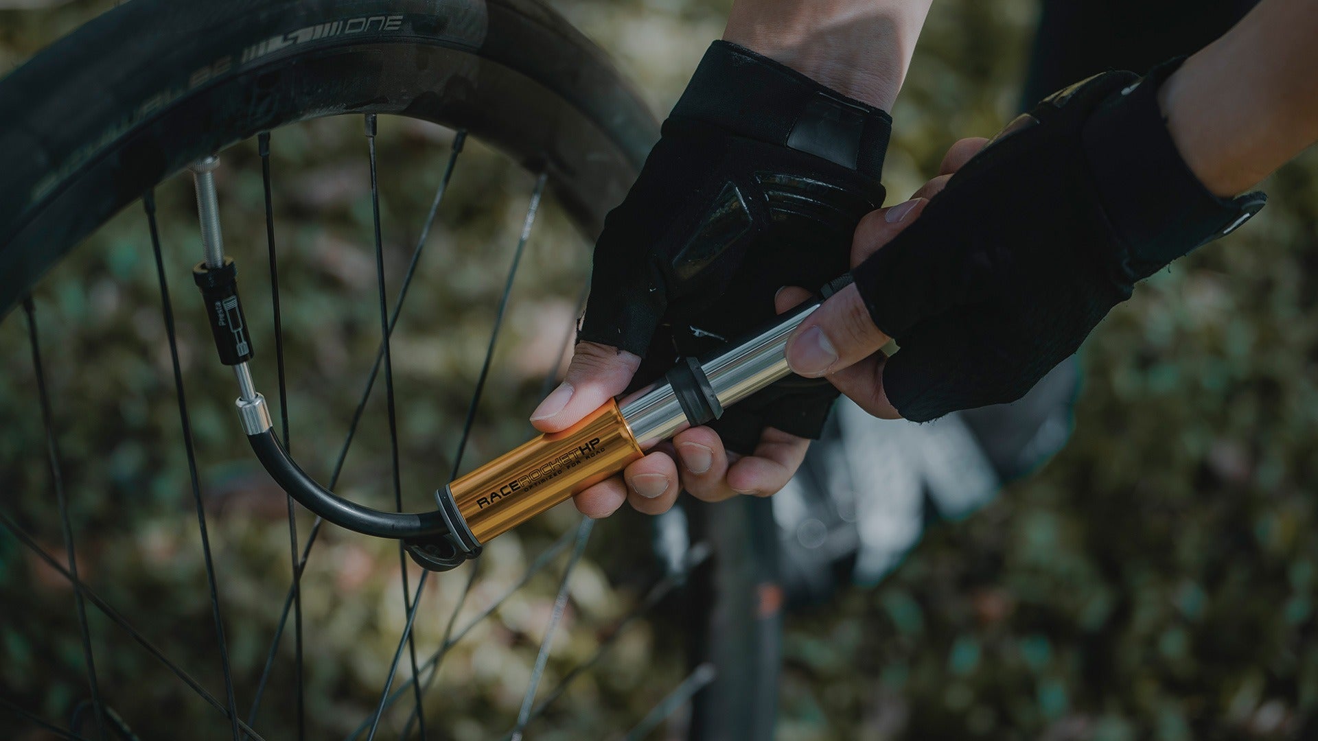 Person using a bike pump to inflate a bicycle tyre outdoors.