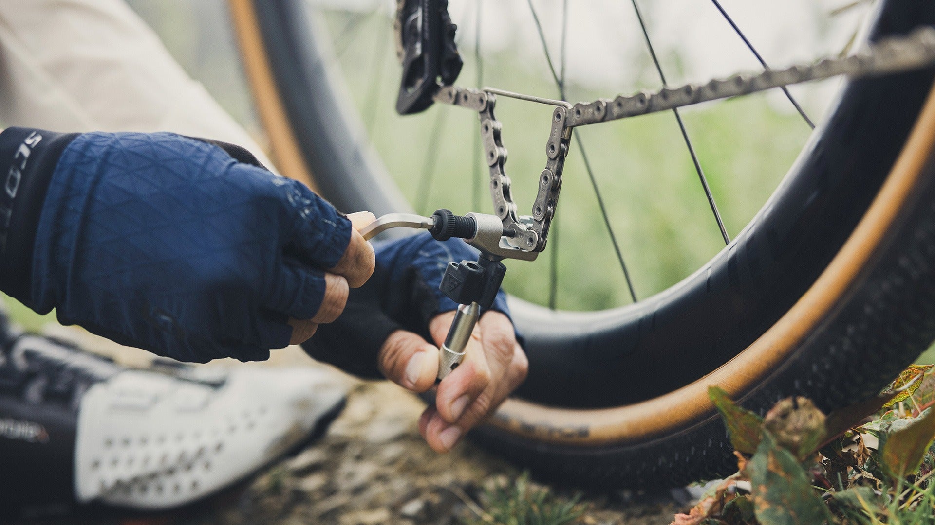 A person using a Topeak Chain Breaker on a bicycle chain outside on the grass