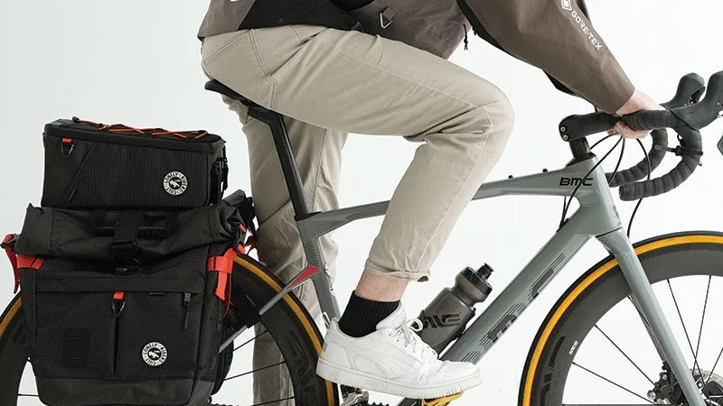Person riding a bicycle with a black pannier bags attached to bike, on a white background