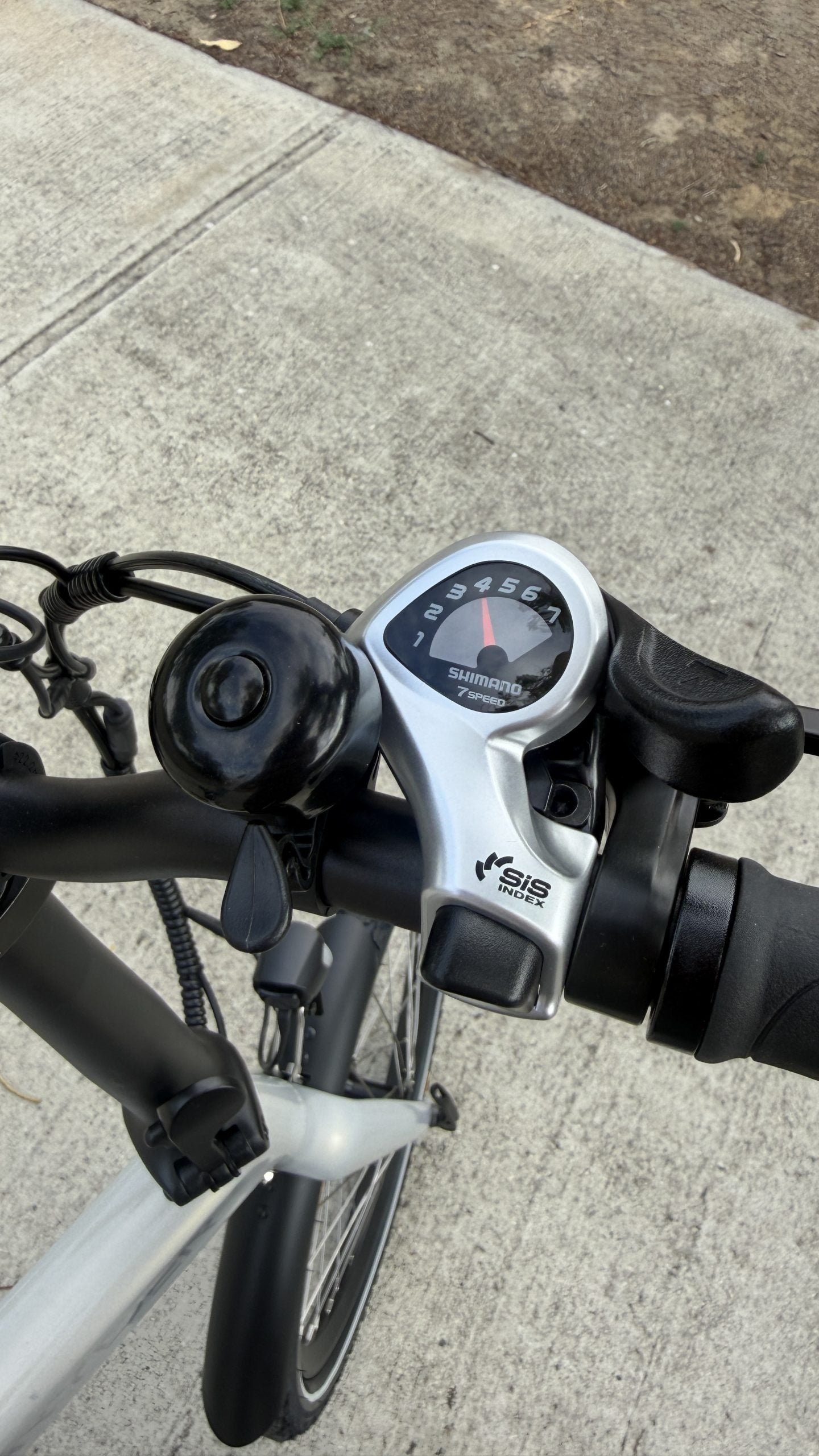 Close-up of a bicycle handlebar with gear levers on a concrete surface.