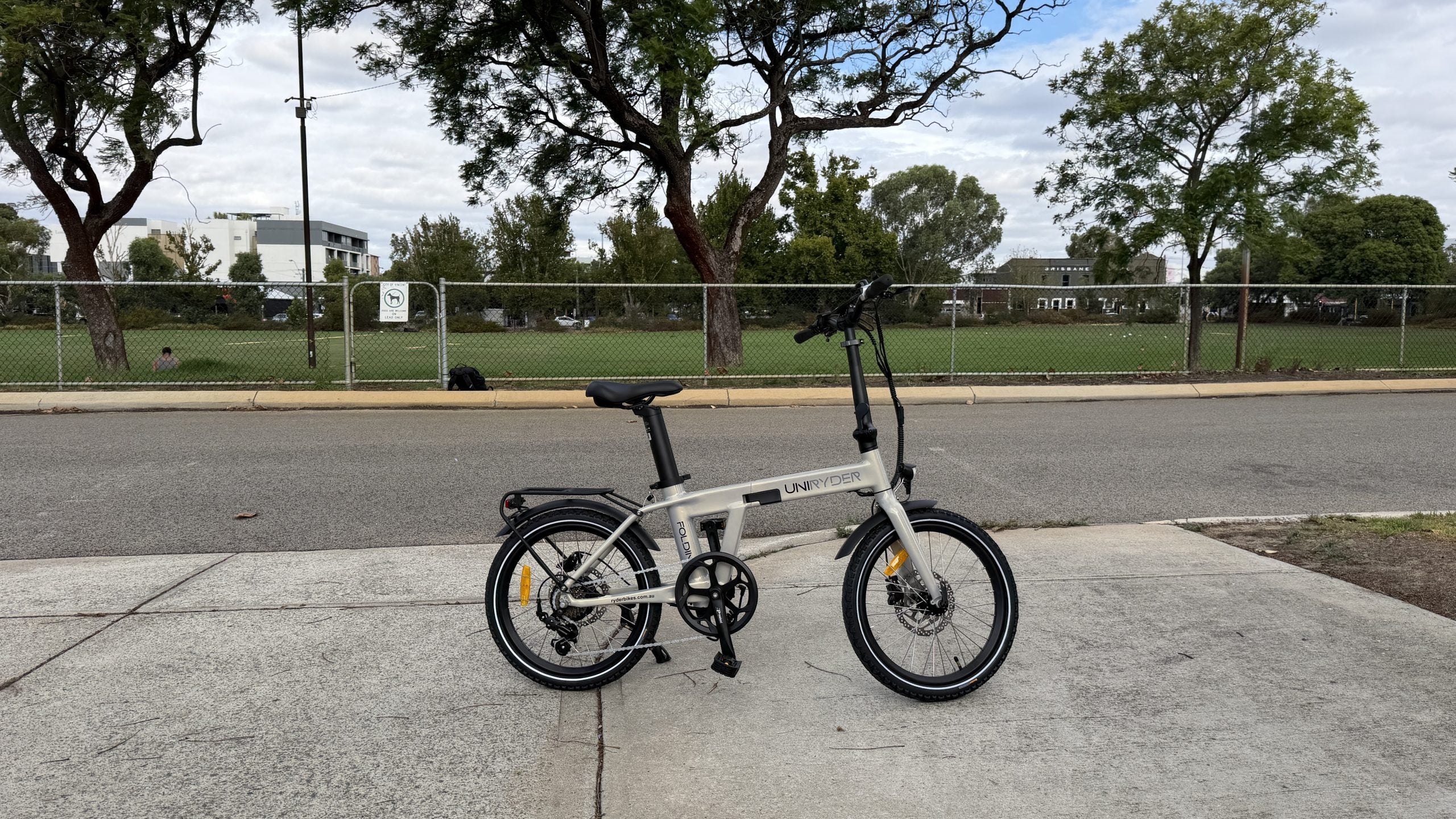 Gray Uniryder folding bike on a sidewalk with a park in the background
