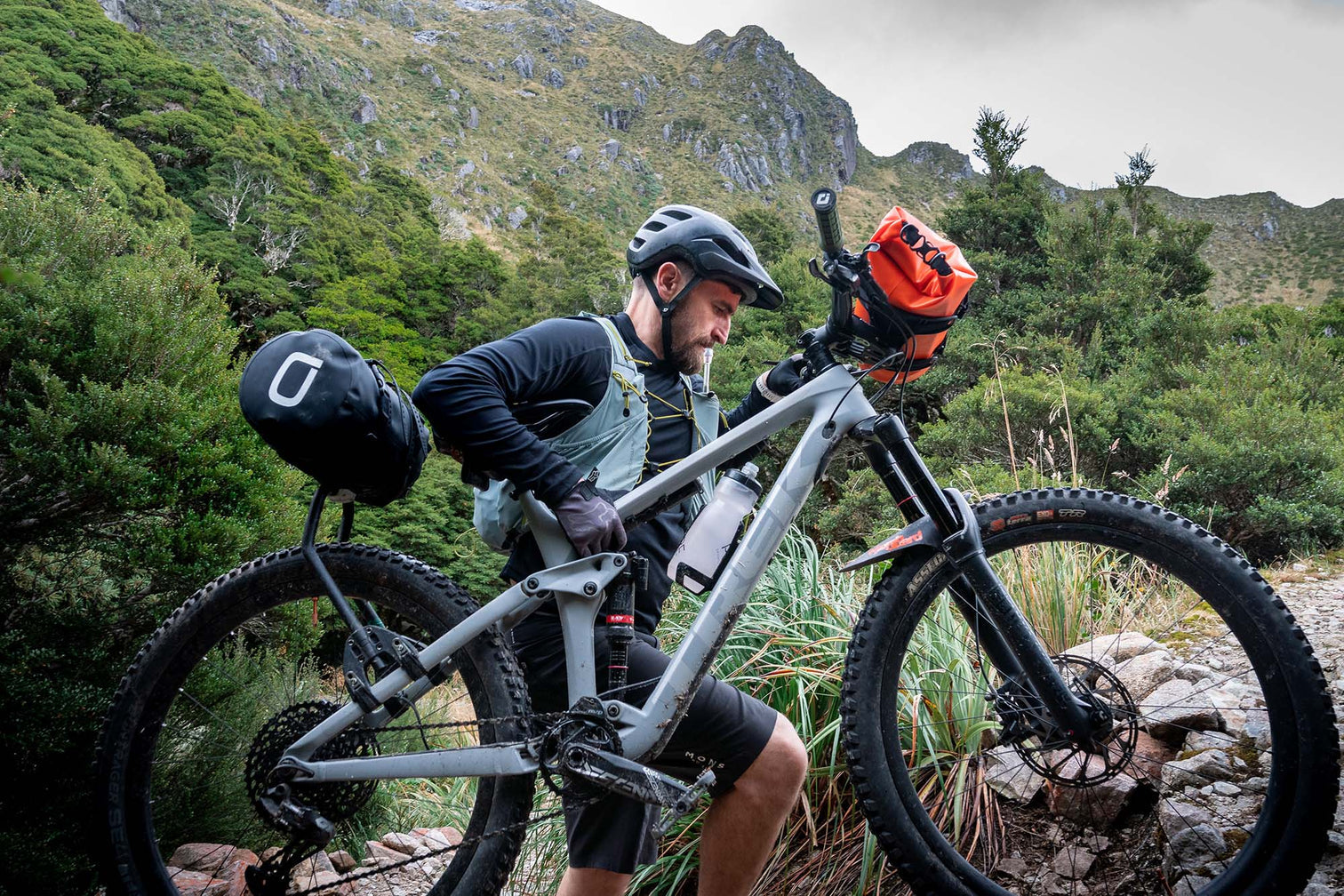 A picture of the Aeroe 12 Litre Dry Bicycle Bag attached to the back and front of a mountain bike being carried by a cyclist