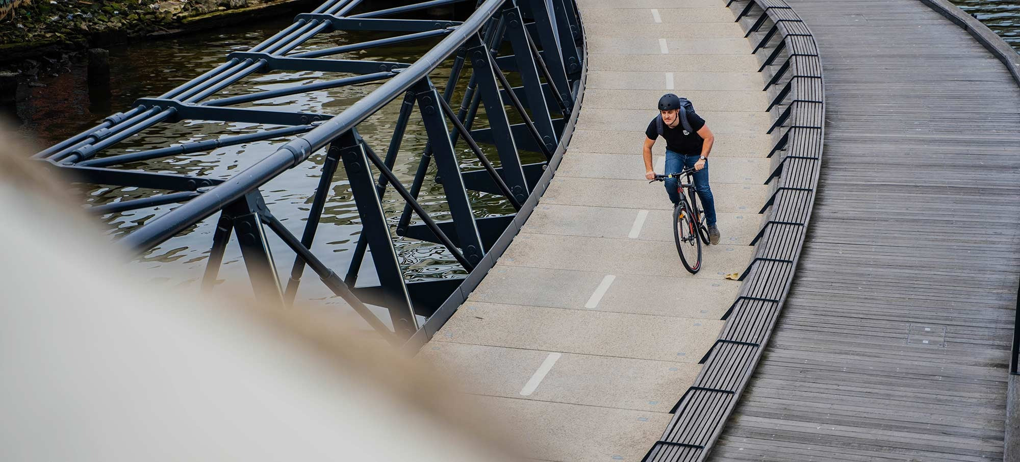 Person cycling on a path next to a body of water with a bridge in the background