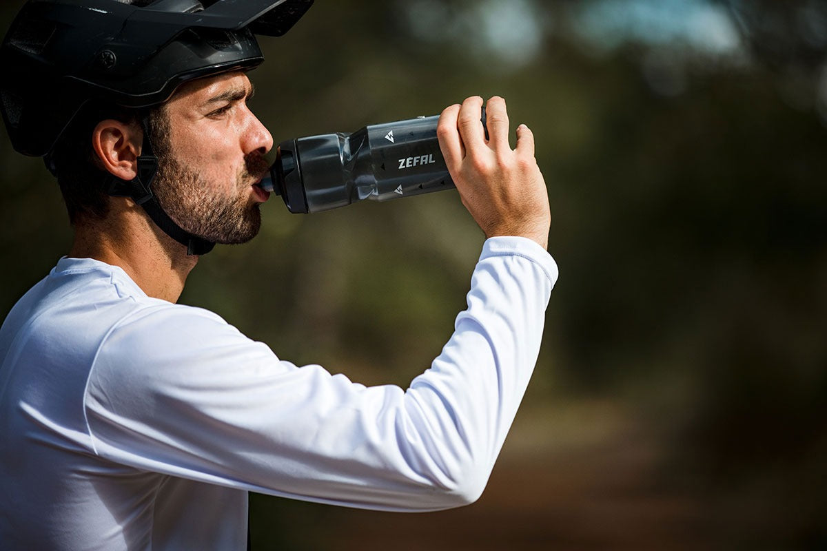 Man drinking from a Zefal water bottle while wearing a mountain bike helmet.