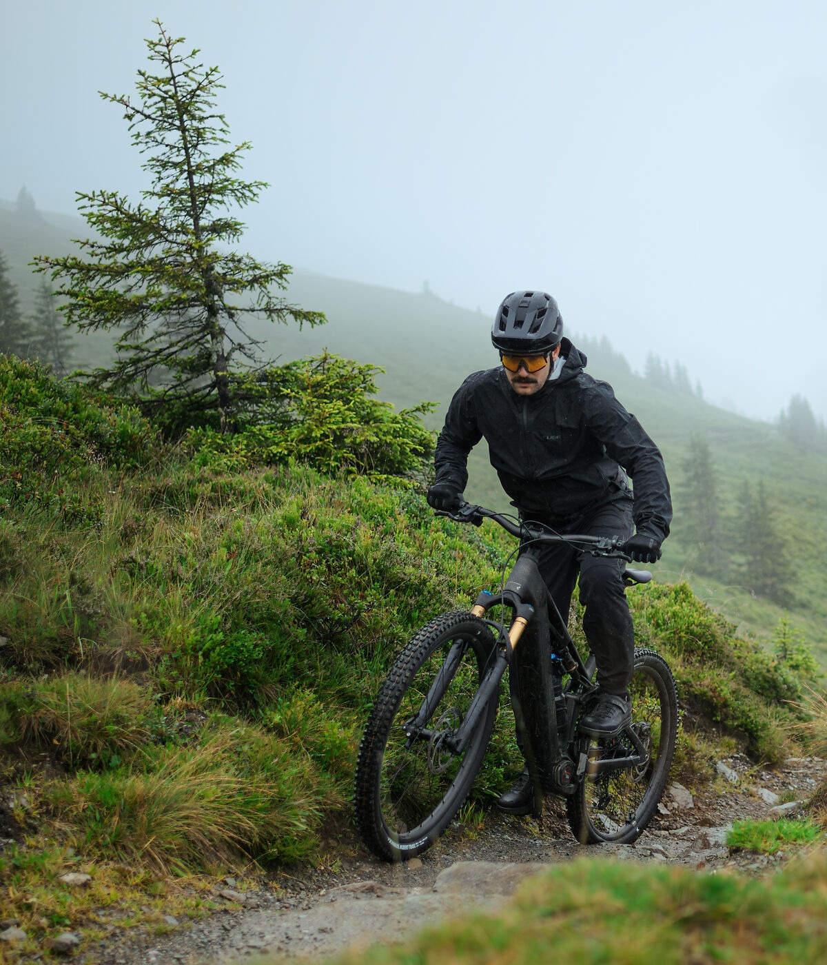 Person mountain biking on a trail in a forested area with foggy conditions